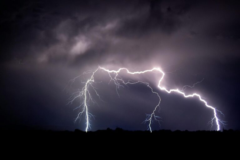Vivid lightning bolts illuminate the dark night sky over an open field creating a striking natural display.