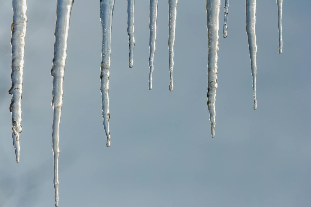 Detailed view of icicles hanging against a clear blue winter sky, showcasing frosty textures.