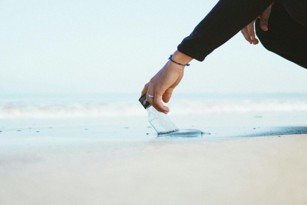 A person reaching down to pick up a bottle on a sandy beach in Morocco.
