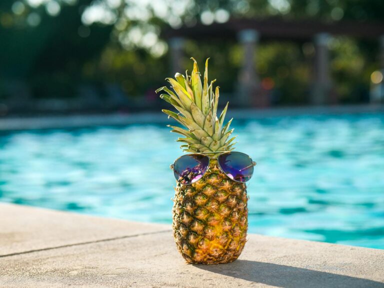 Tropical pineapple wearing sunglasses by a sunny swimming pool, perfect for vacation vibes.